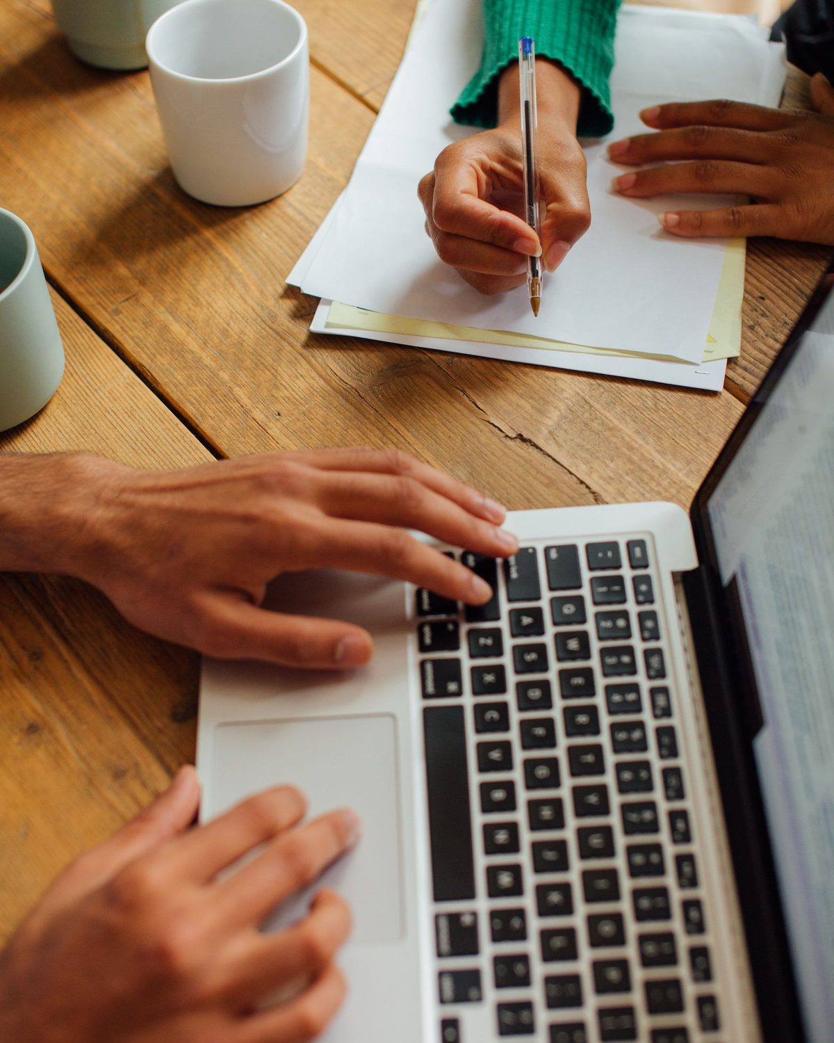 Hands on a laptop keyboard and handwritten notes on a wooden table